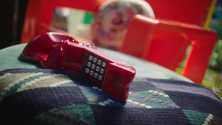 A red wire telephone and on top of a cloth that is on a table