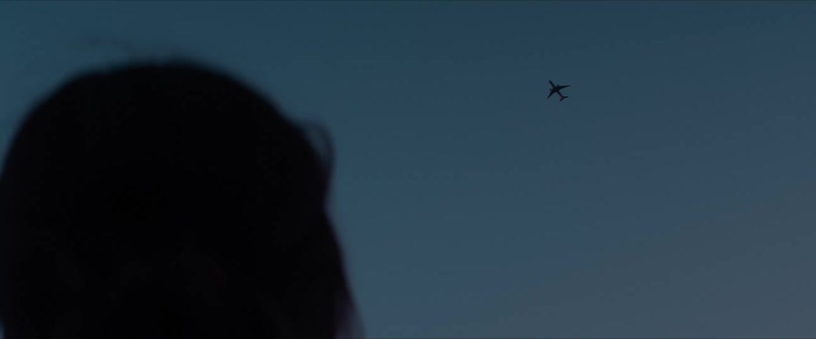 Silhouette of a woman watching a plane flying in a dark dawn sky