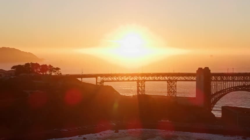 Sun glares across bridge and nearby coastal town from a red horizon