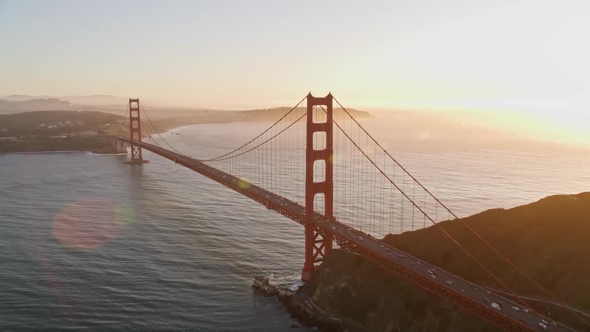 Aerial scene of the golden bridge over the sea with mountains around and the suns reflection on the horizon