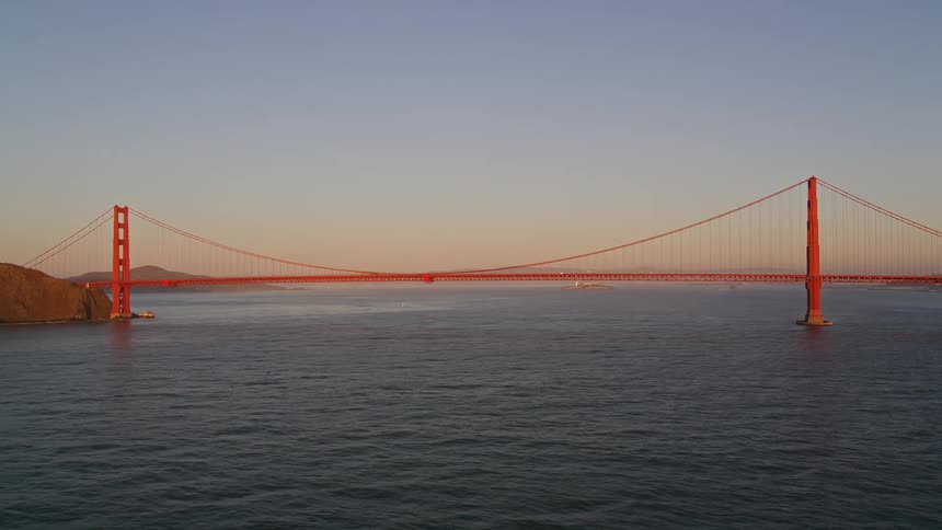Golden gate bridge crosses water against a red tinted horizon
