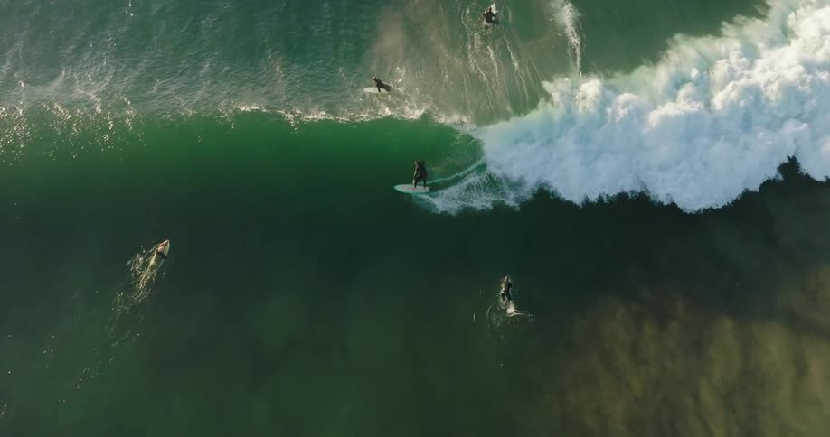 Top view of people in the middle of the sea with one of them surfing a wave