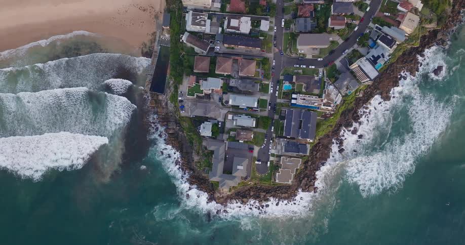 Aerial view of a cluster of luxury homes situated on a narrow strip of land between the ocean and a beach
