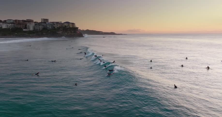 People in the sea with some of them surfing a wave on a morning with a red sky
