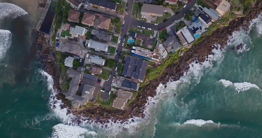 Aerial view of a cluster of luxury homes situated on a narrow strip of land between the ocean and a beach