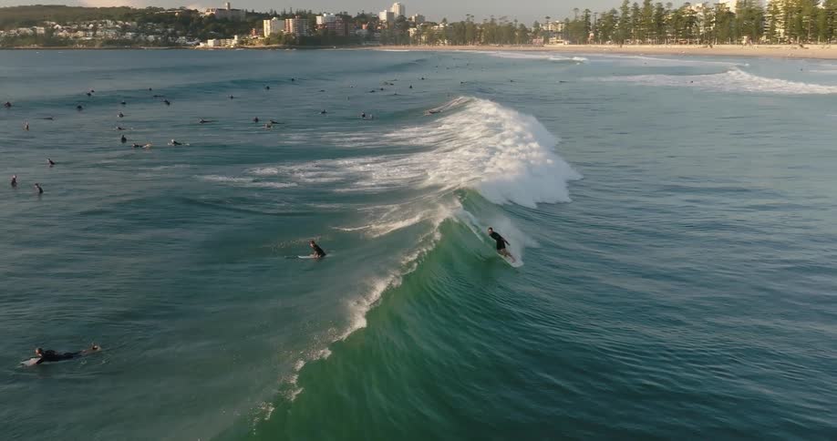 Surfers surf in ocean near beach bordering a small city