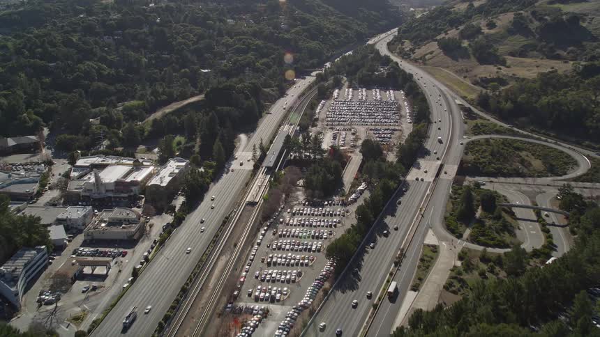 Aerial panorama of two highways in opposite directions with vehicle traffic and central overpass with parking lot