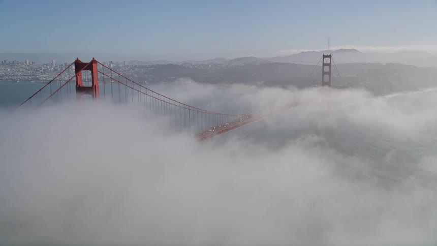 Aerial panorama of a mountain in fog and overlooking a bridge over the sea with metropolises on the horizon