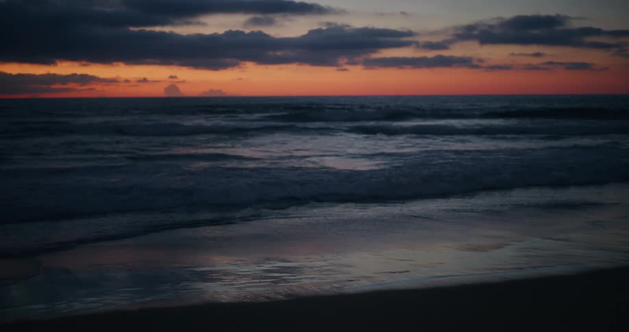 Panorama of a beach with calm waves and a red sky on the horizon