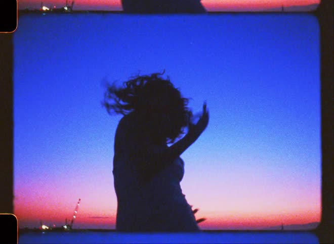 Silhouette of a woman on the beach dancing against a blue and reddish sky on the horizon