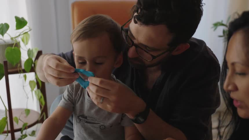 Father and mother sitting at a table and playing with their son with modeling clay