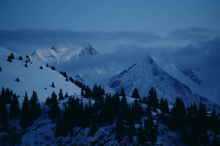 Low lying clouds pass over snow covered mountain range after dusk
