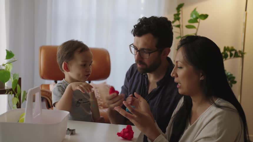 Father and mother next to their young son playing with modeling clay indoors in the living room