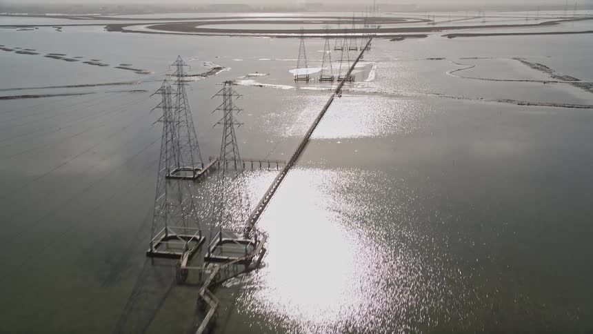 Aerial panorama of power transmission towers amidst a water reservoir with solar reflection