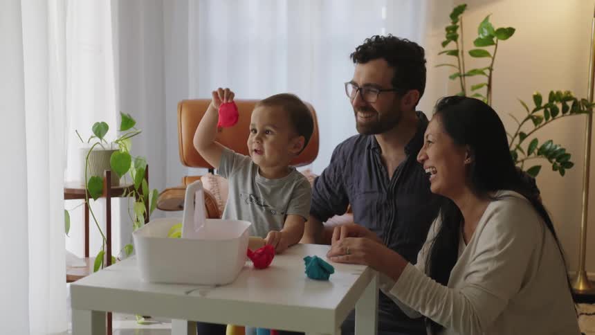 Father and mother smiling while one plays with their son with modeling clay