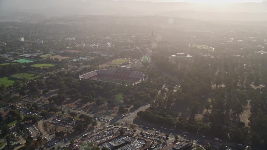 An aerial view of a sports stadium next to a busy highway and with bright sunlight from the sky