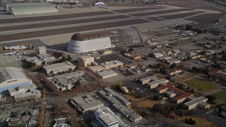 Aerial panorama of an airstrip with industrial warehouses around it and an urban city in the background