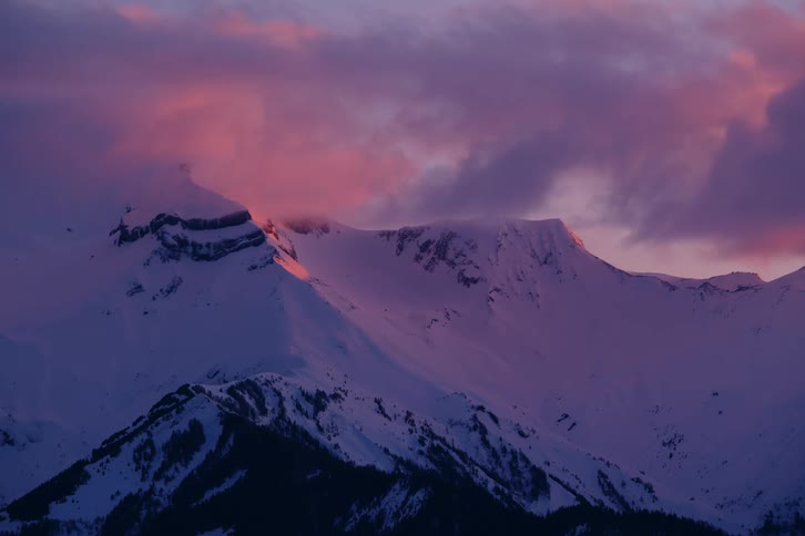 Red tinted clouds flow over a snow covered mountain