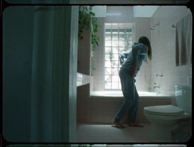 A man with long hair takes off his light blue hoodie to bathe in the bathroom