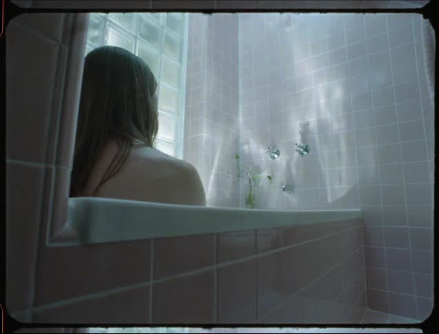 Man sitting in a tiled bathtub with water reflection on the walls