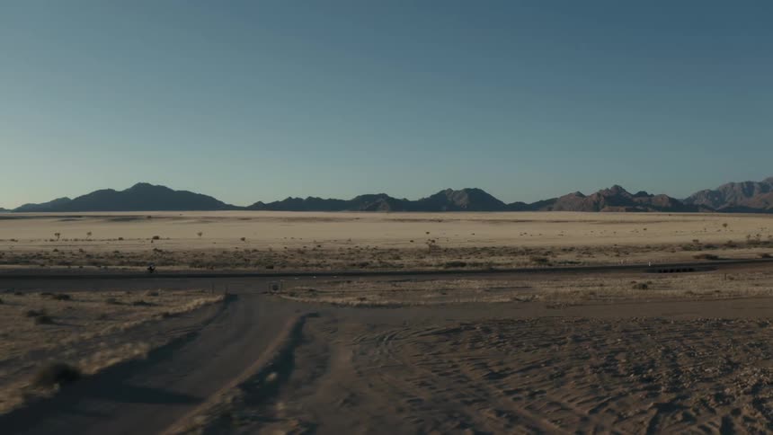 Panorama of desert vegetation with mountains on the horizon and a person cycling on a narrow asphalt street