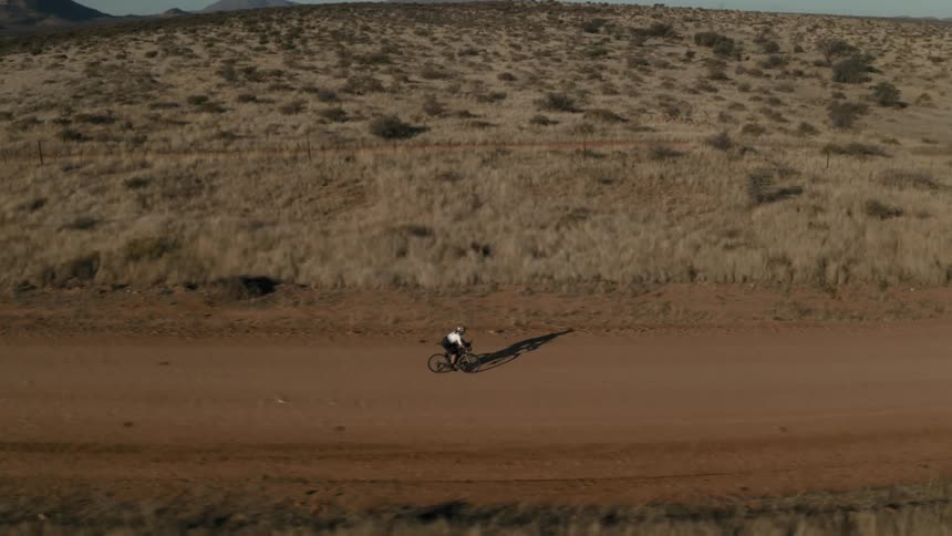 Person cycling on a dirt road surrounded by desert vegetation on a clear day