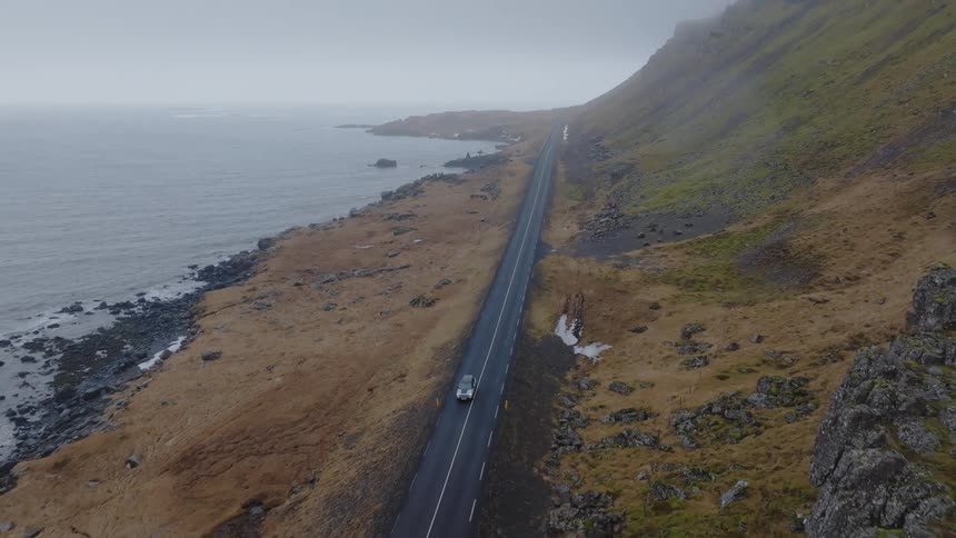 Aerial panorama of a vehicle traveling on a paved street by the sea and next to a mountainous coast