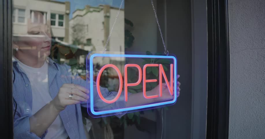 A female employee straightens and turns on the neon open sign in a business