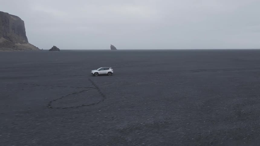 White suv car driving on a dirt road with mountains on the horizon on a cloudy day