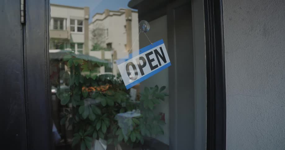A young woman turns a sign from closed to open