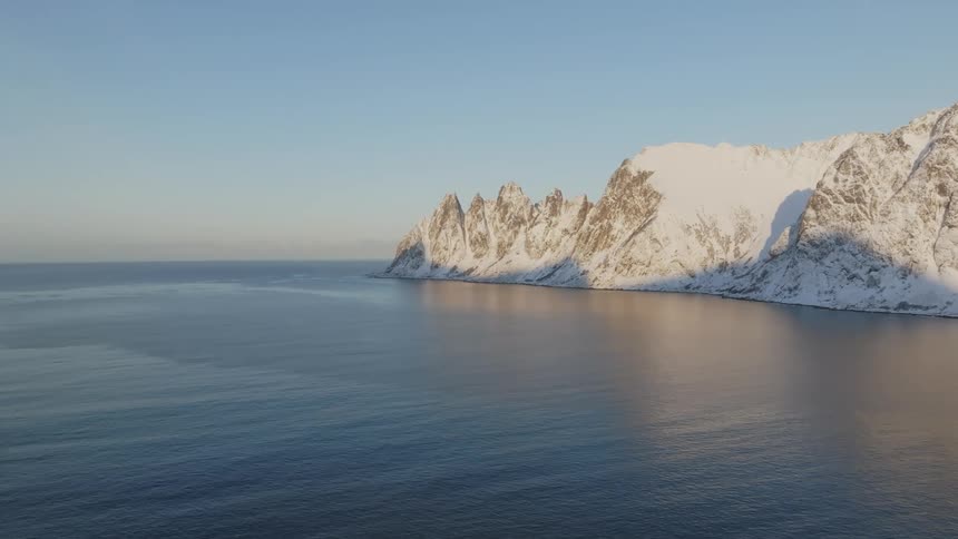 Water flows by a snow covered mountain coast