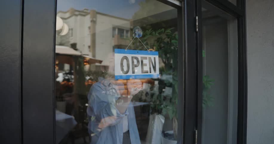 A female employee turns a closed sign to open in a business