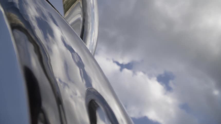 The sky and clouds are reflected on a metallic structure