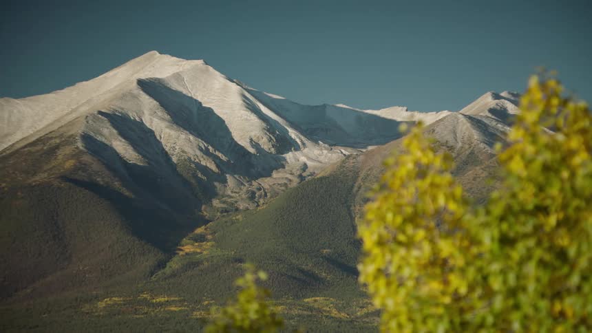 Snow is dusted on the tops of the mountain peaks behind leafy trees