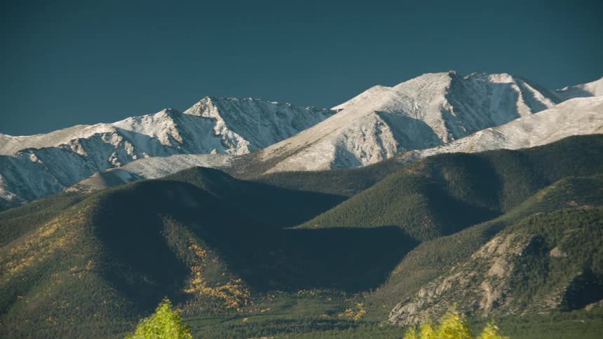 Wooded and snowy mountain range on a cloudless blue sky day