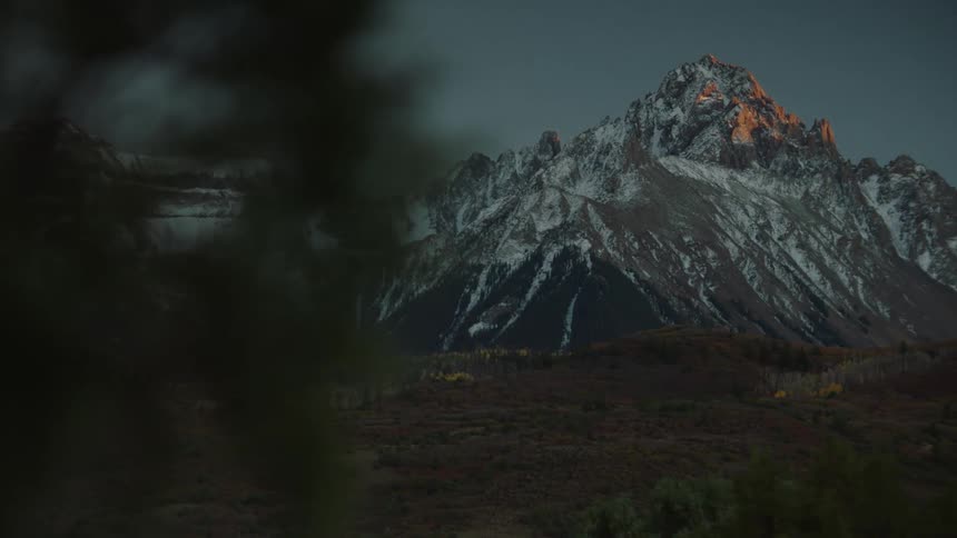 A rugged mountain peak with snow and the last light of sunset hitting its peak