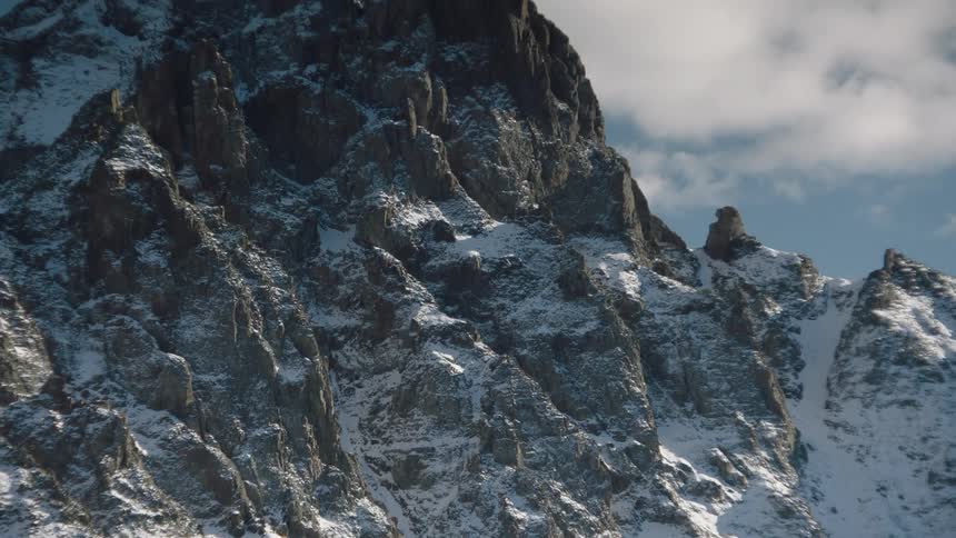 Mountain with cliff covered in snow on a blue sky day with clouds