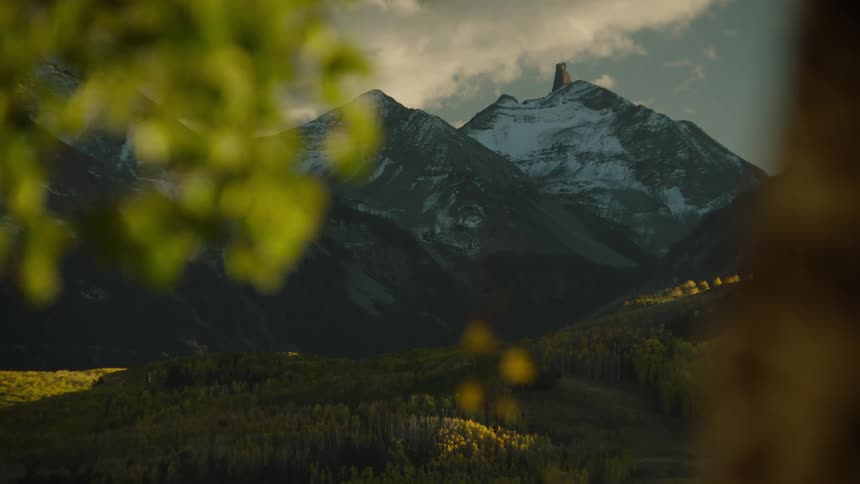 Scenery of hills greened by forests and snowcovered cliffs in the background