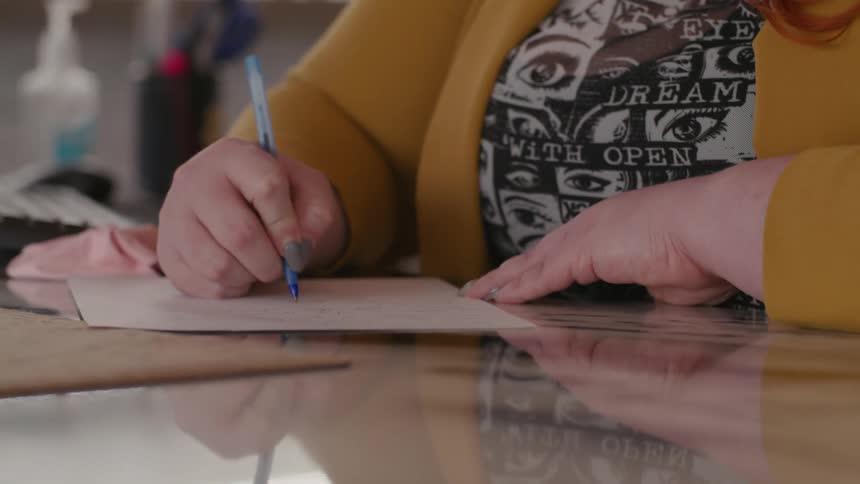 Woman writes on paper with a blue pen in a kitchen