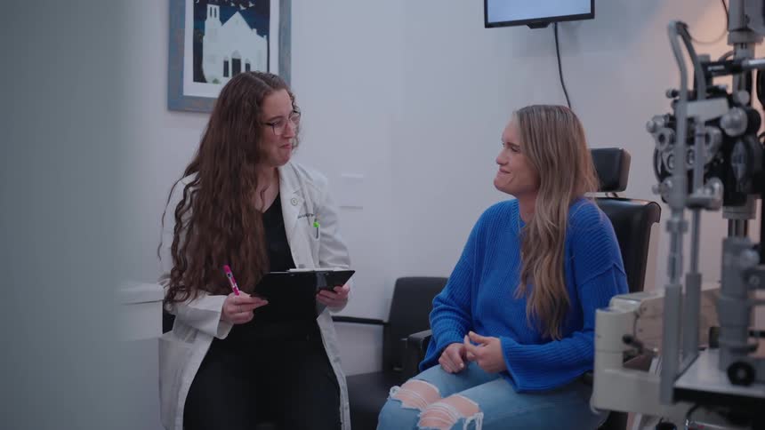 Woman in a lab coat and with a clipboard talking to a patient who is sitting on the chair in an office