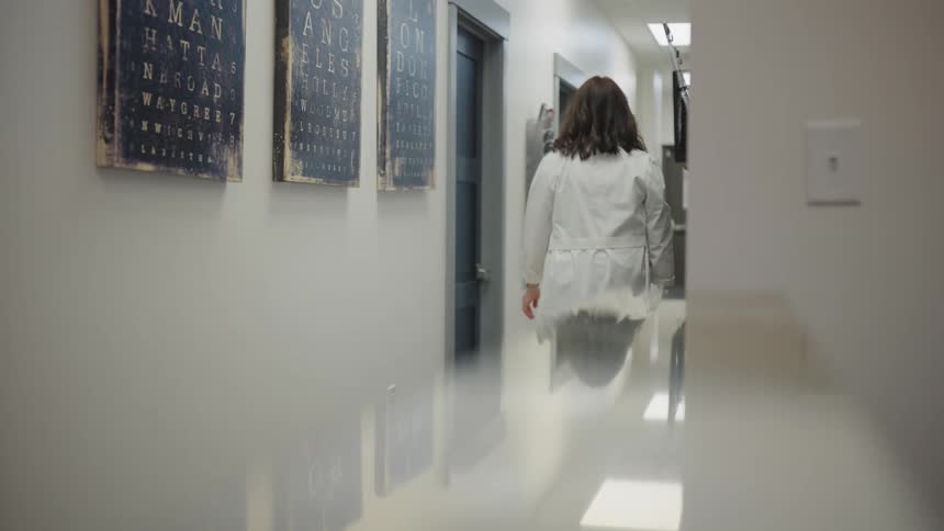 Woman in a lab coat walking down an office hallway