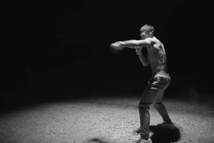 Male boxer shadow boxes while standing under circle of light outside at night