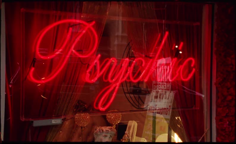 Neon sign in psychic store window reflects nearby outdoor environment