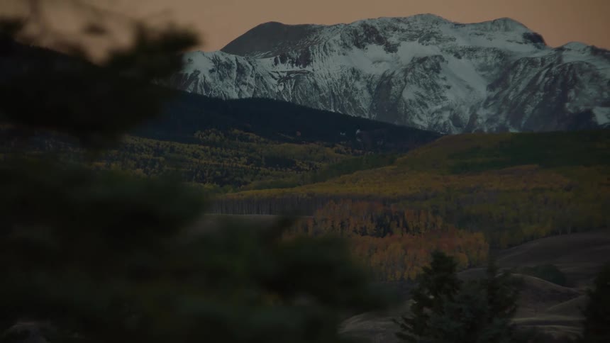 A mountain covered stands tall behind grass covered hills