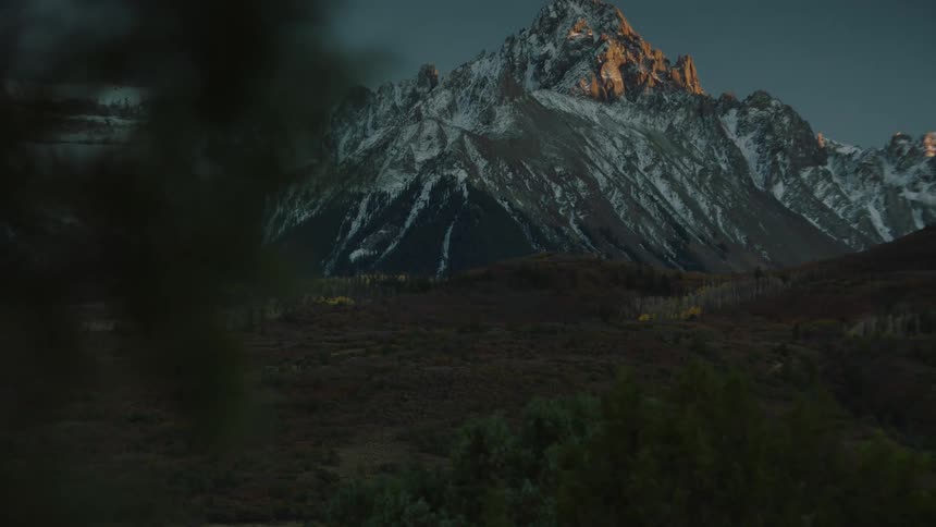 Snowcapped mountain towers over a forest at sunset