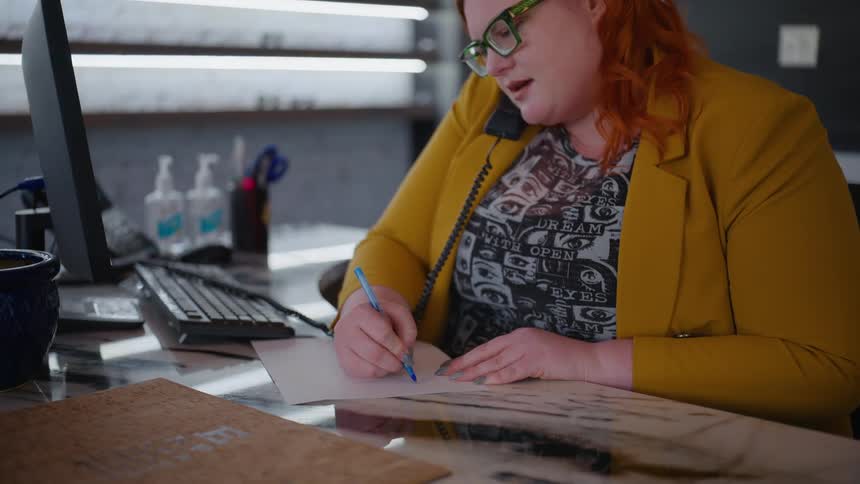 Woman on the phone making a note on a paper while working in the office