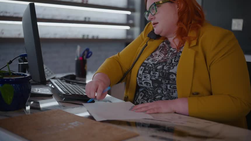 A woman working at the office takes notes while having a call