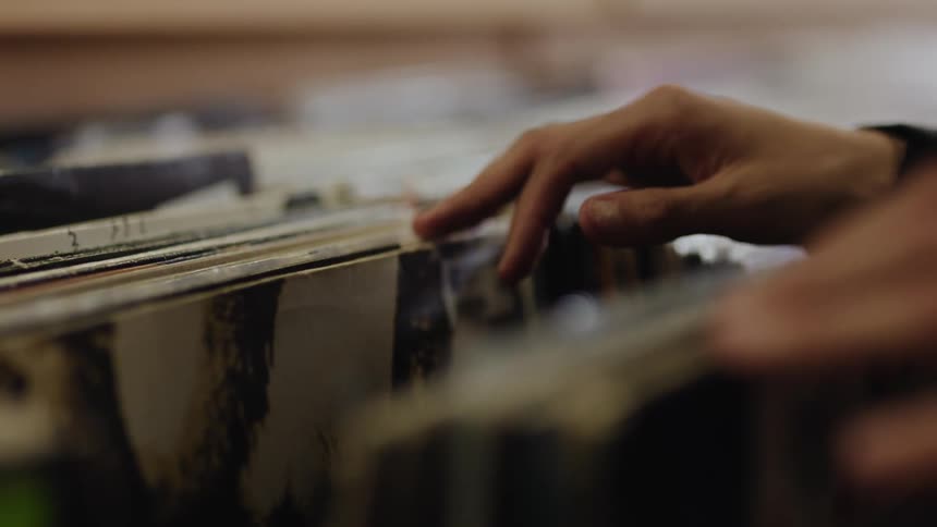 A closeup of a hand browsing through a collection of vinyl records