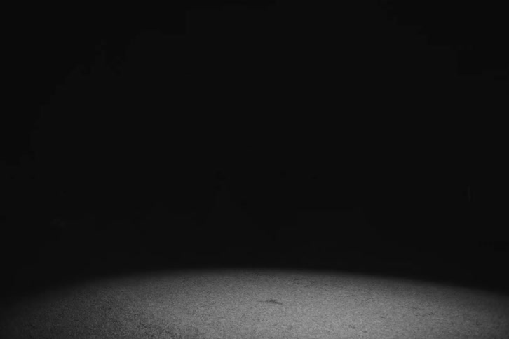 A light briefly illuminates the ground as a person walks in the pitch black background