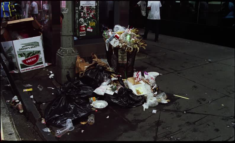A pile of garbage on a city street corner with overflowing trash bags and litter scattered around